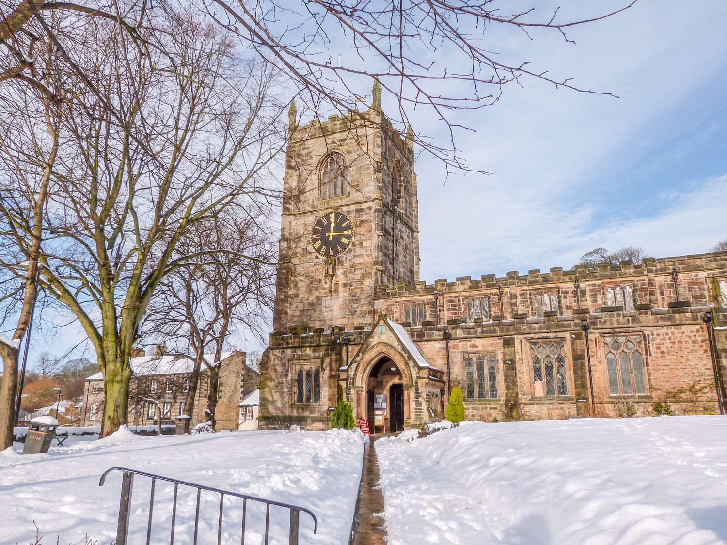 Un edificio histórico de piedra con una alta torre de reloj, un patio cubierto de nieve y un estilo arquitectónico tradicional.