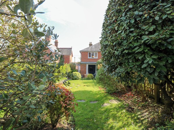 A residential garden with a brick house, a hedge, and a lawn.