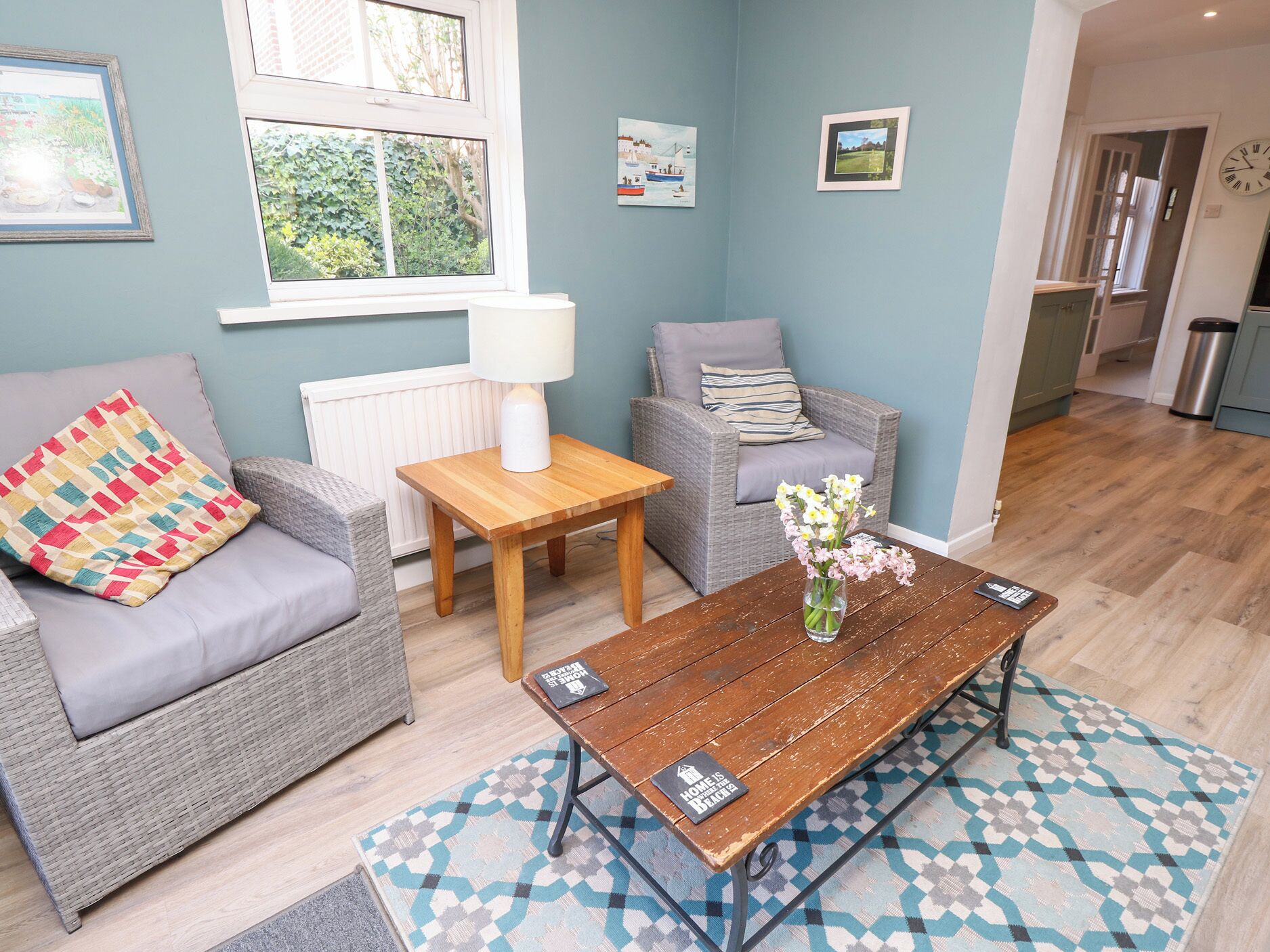 A cozy living room with a sofa, armchair, and coffee table, featuring a small table lamp and a vase with flowers.