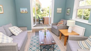Una sala de estar acogedora con muebles de mimbre, un tapete estampado y vistas a un patio exterior a través de un ventanal.