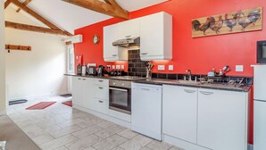 A modern kitchen with white cabinets, a red accent wall, and a wooden ceiling. - The Hen House (Diss)