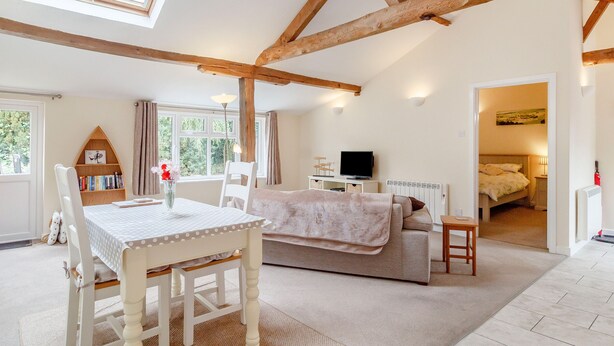 A cozy room with a wooden ceiling, a dining table with chairs, a sofa, a TV, and a bookshelf. - The Hen House (Diss)