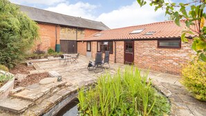A brick building with a tiled roof, a patio with chairs, and a small water feature. - The Hen House (Diss)
