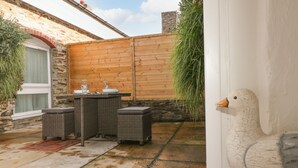 Une terrasse avec des meubles en osier, un mur blanc orné d’une sculpture de canard et une clôture en bois.
