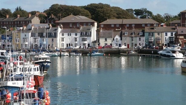 A marina with boats docked, surrounded by multi-story residential buildings. - Buccaneer Cottage (Weymouth)