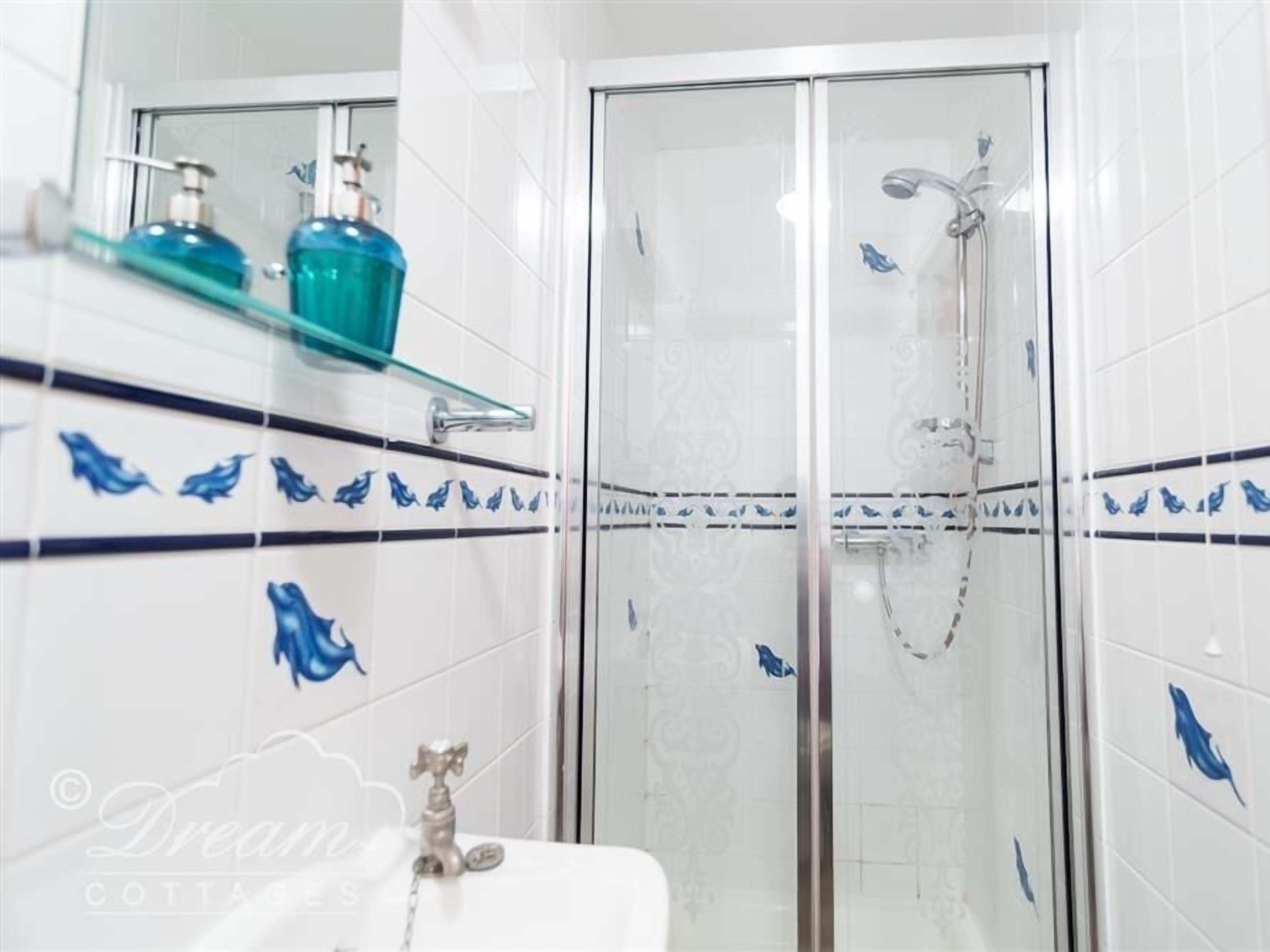 A bathroom with white tiles, a glass shower enclosure, and a shelf with toiletries.
