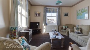 A cozy living room with a television, a dining table with a bowl of fruit, and a sofa. - Buccaneer Cottage (Weymouth)