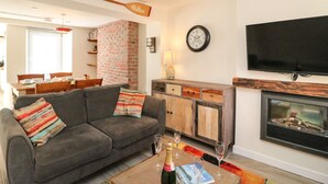 A living room with a gray sofa, a wooden cabinet, a fireplace, and a flat-screen TV mounted on the wall. - Anchor Cottage (Weymouth)