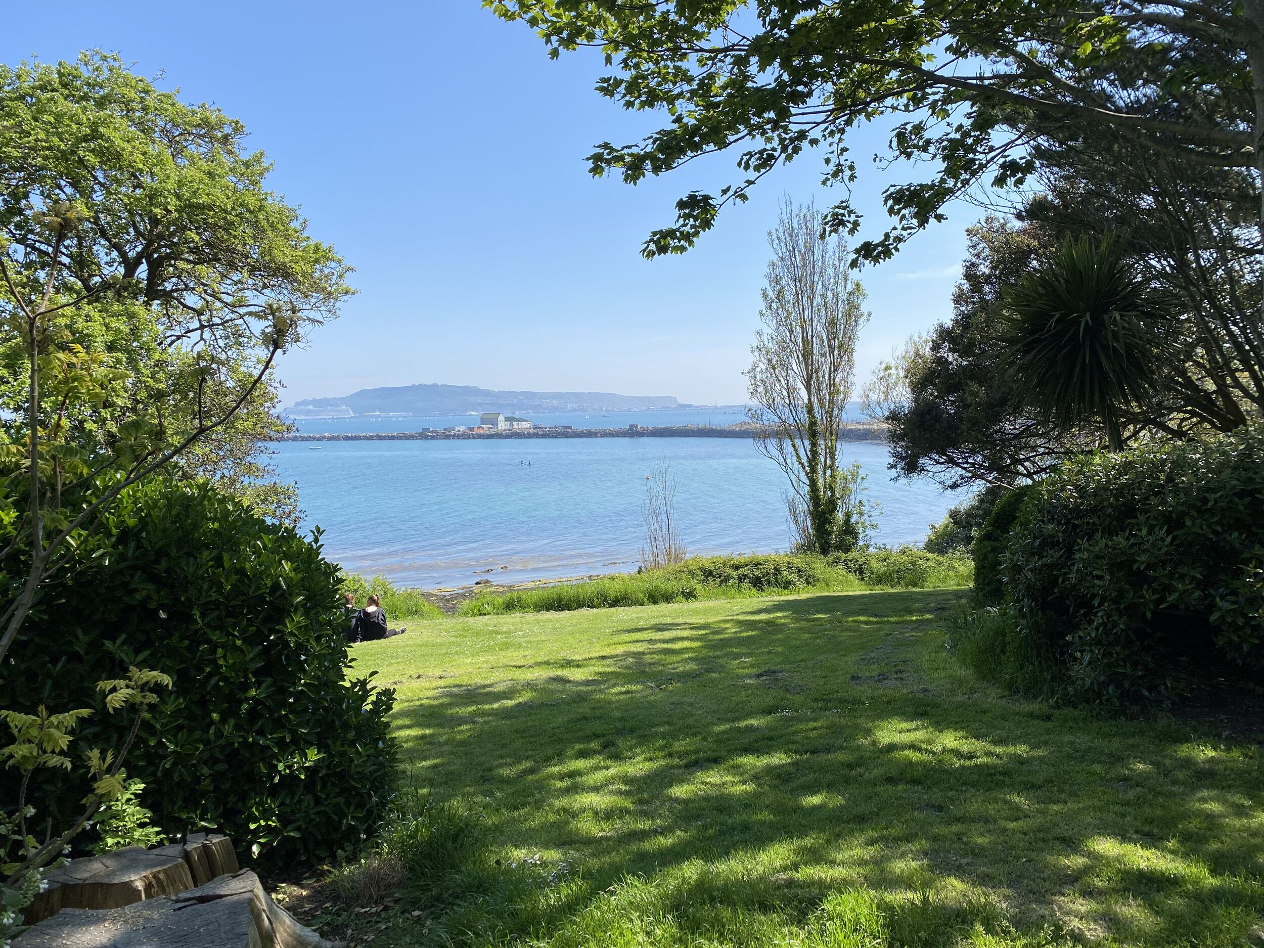 A grassy area with a view of a calm body of water and distant landforms.