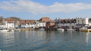 A harbor with boats docked, buildings along the waterfront, and a clear sky. - Anchor Cottage (Weymouth)
