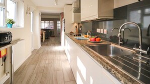 A modern kitchen with a long countertop, stainless steel appliances, and a view into the dining area. - Anchor Cottage (Weymouth)