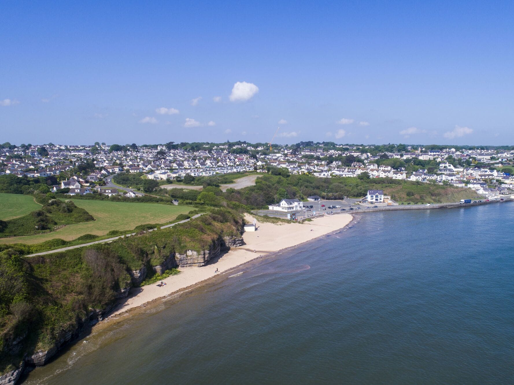 A coastal town with a sandy beach, a rocky shoreline, and a dense residential area in the background.