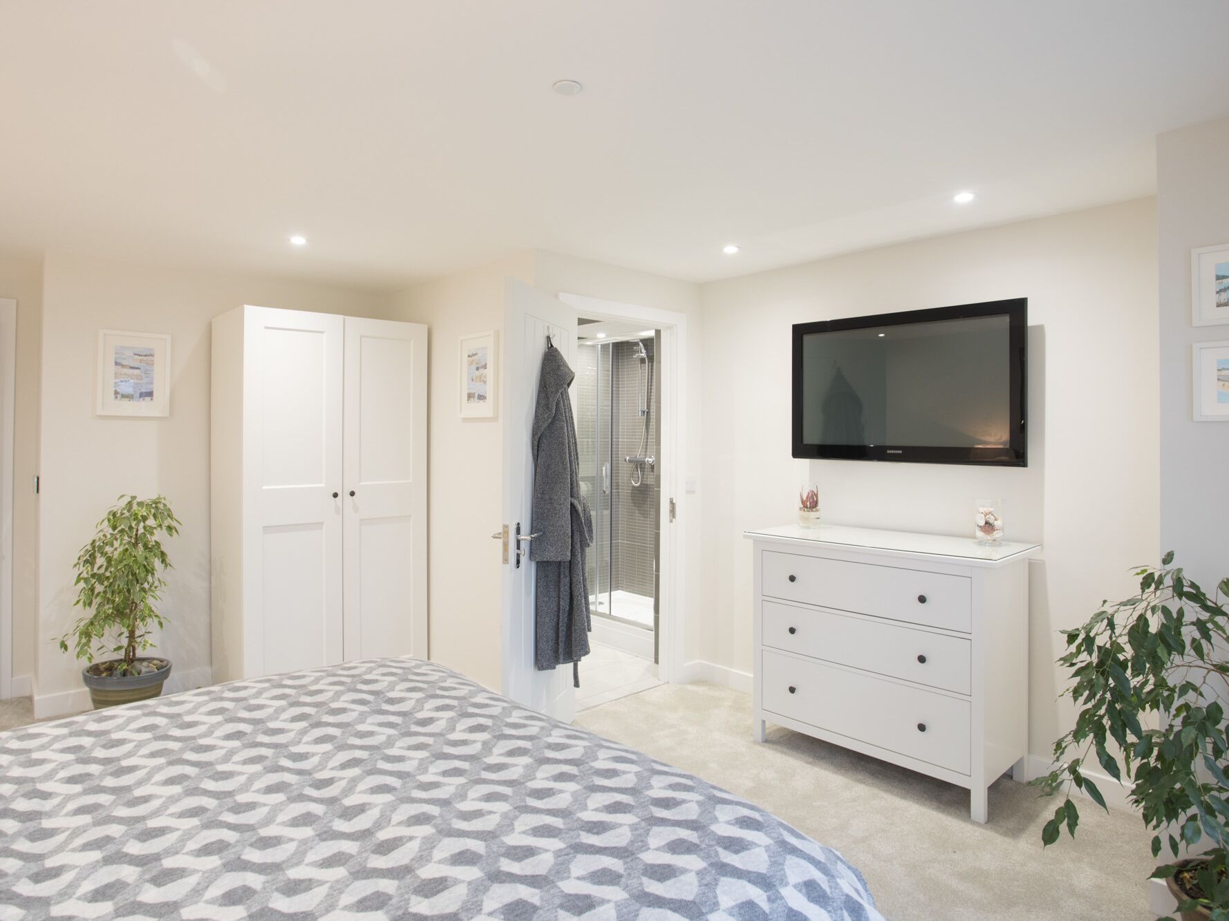A bedroom with a bed, a TV, a dresser, and a door leading to a bathroom.