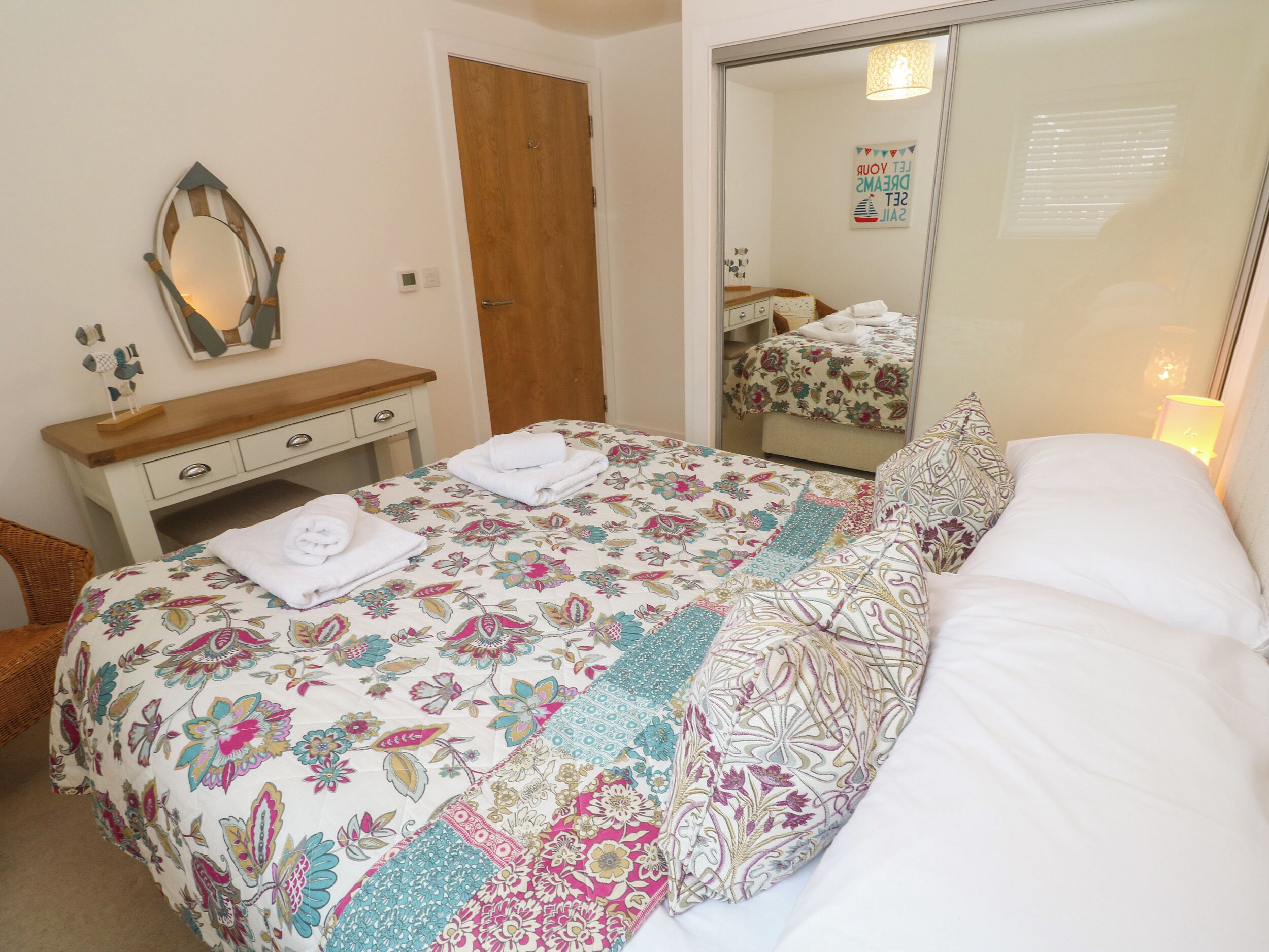 A bedroom with a bed, a wooden dresser, a mirror, and a door.