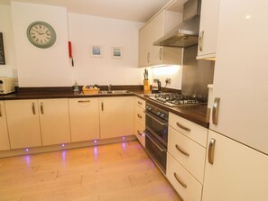 A kitchen with a stove, oven, and sink. There are cabinets, a clock, and a coffee maker. - Ocean Seven (Newquay)