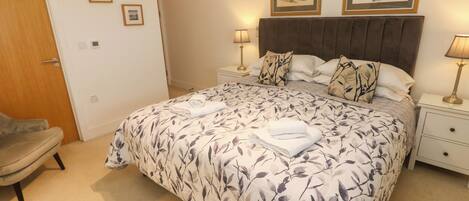 A neatly made bed with a floral bedspread, two bedside lamps, and a headboard with a dark wood finish.