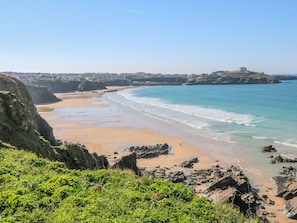 Un paysage côtier avec une plage de sable, des affleurements rocheux et un bâtiment situé au loin, sur une colline.