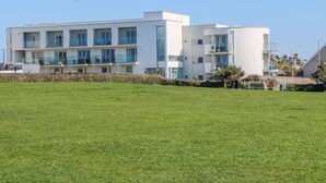 A modern multi-story building with balconies, a flat roof, and a grassy area in front. - Ocean Seven (Newquay)