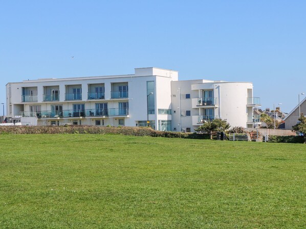 Un immeuble moderne à plusieurs étages, doté de balcons, d’un toit plat et d’un espace verdoyant à l’avant.