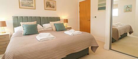A neatly made double bed with pillows, a bedside table with a lamp, and a door to another room.