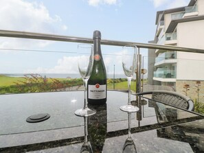 A bottle of Taittinger champagne and two glasses on a glass table with a view of a building and landscape. - Ocean Seven (Newquay)