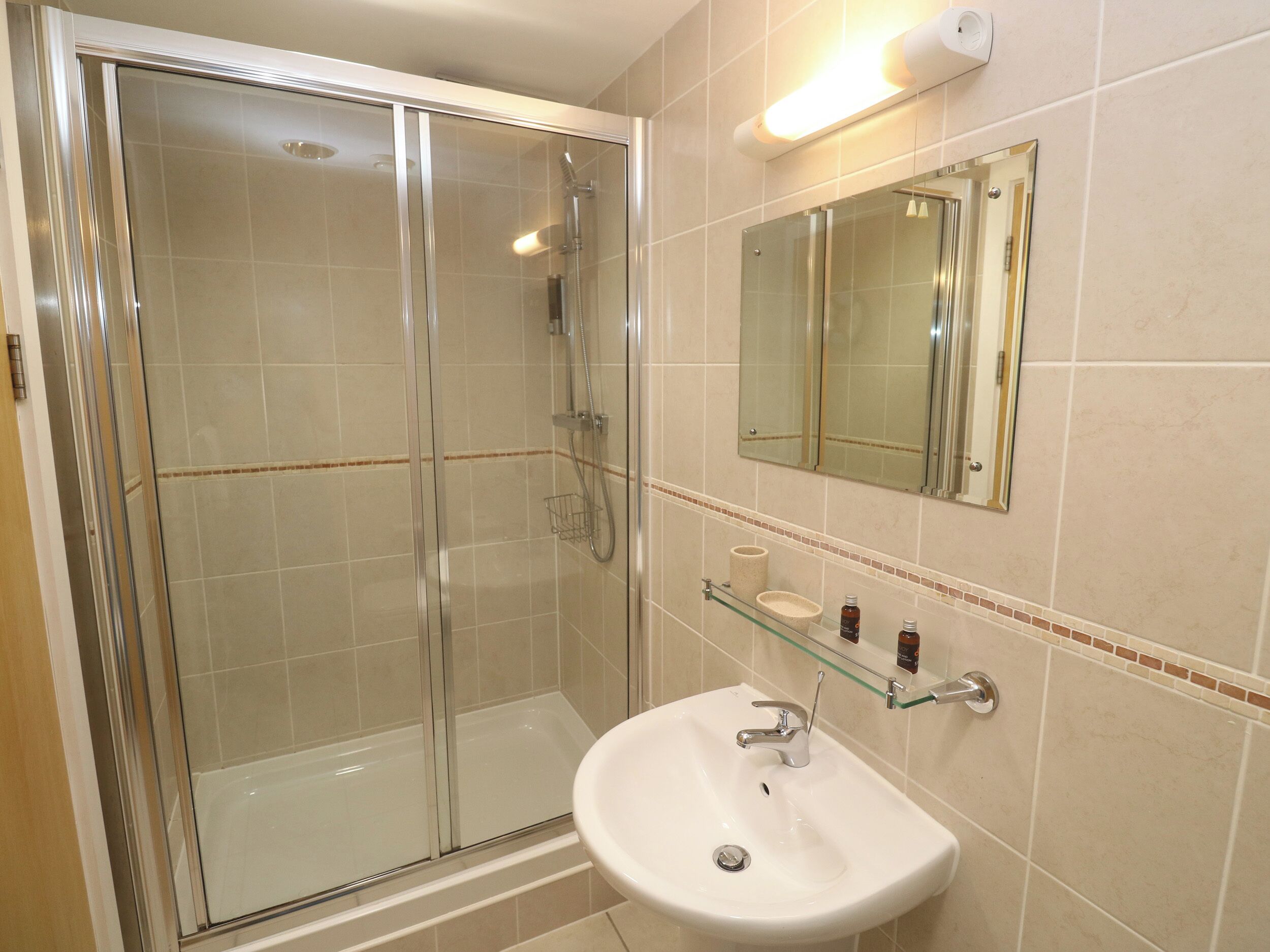 A bathroom with a glass-enclosed shower, a white sink, and a mirror above it.
