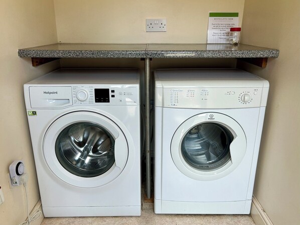 Two front-loading washing machines, one Hotpoint and one Indesit, in a laundry room with a countertop above. - The Stables (Buxton)