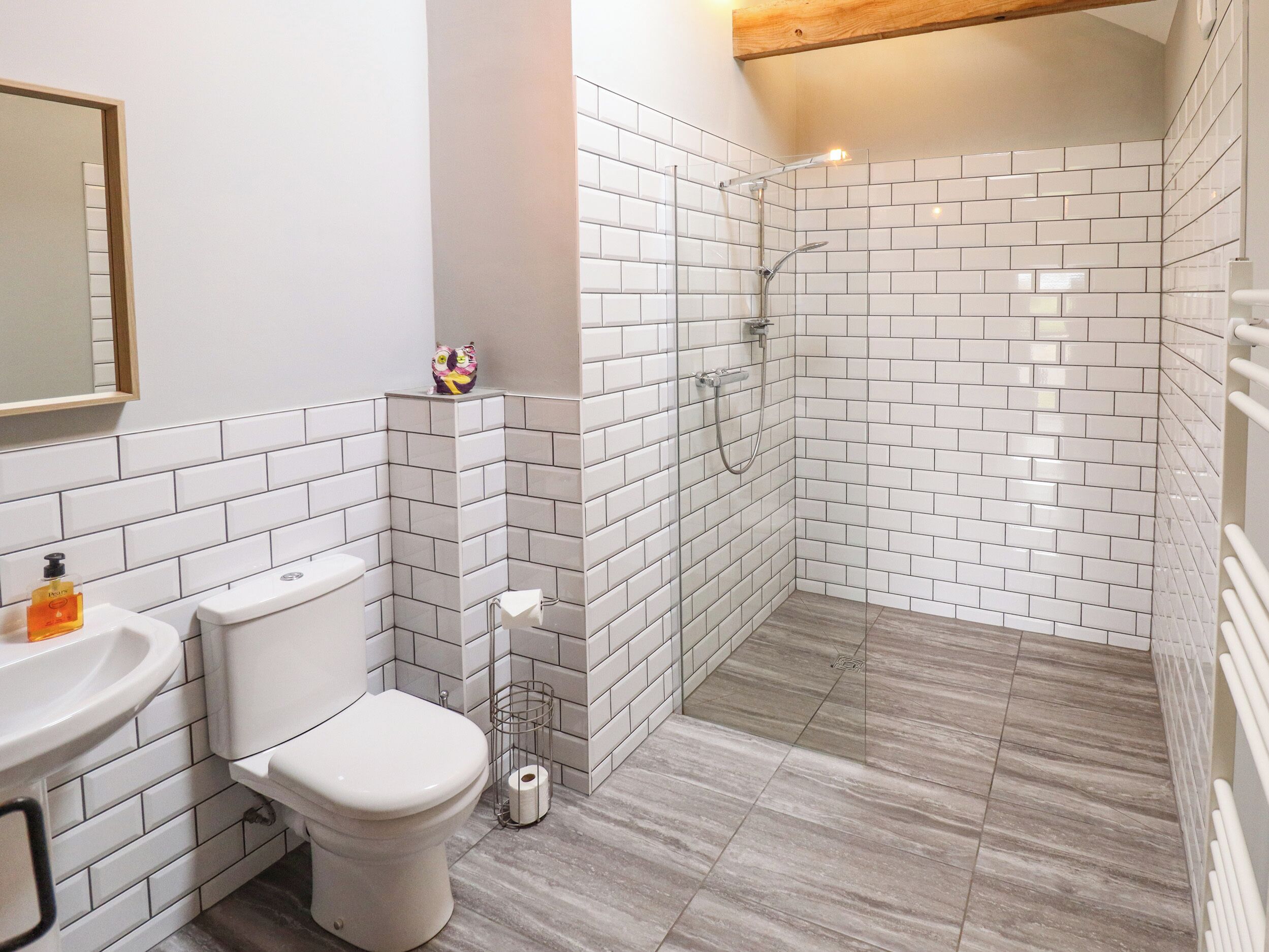 A bathroom with white tiled walls, a toilet, a sink, and a shower area.