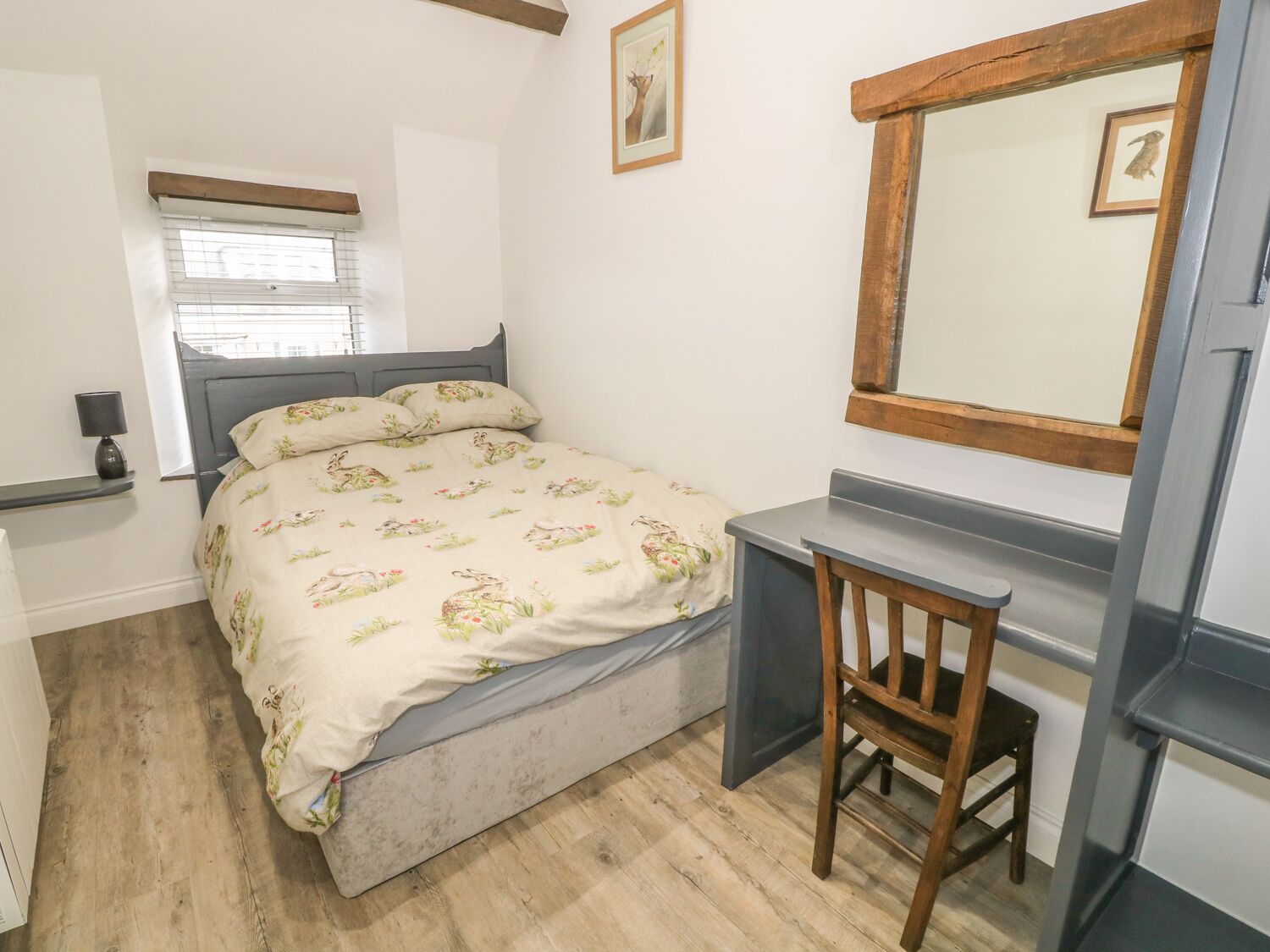 A bedroom with a bed, a desk, a chair, a window, and a mirror.