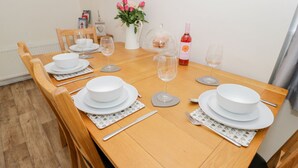 A dining table set with white plates, bowls, and cutlery, a vase with pink flowers, a wine bottle, and a clear glass. - 5 Ceirnioge Cottages (Betws-Y-Coed)