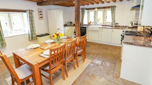 A cozy kitchen with wooden beams, a dining table set for four, and a view of the adjacent room. - Woodthorpe Cruck Cottage (Chesterfield)