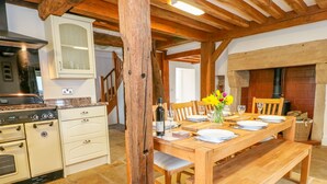 A kitchen with a wooden table set for dining, a stove, and a fireplace. - Woodthorpe Cruck Cottage (Chesterfield)