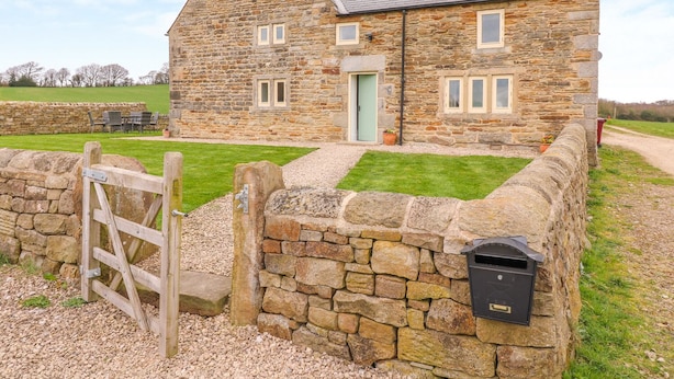 A stone house with a sloped roof, a green door, and a mailbox attached to the wall. - Woodthorpe Cruck Cottage (Chesterfield)
