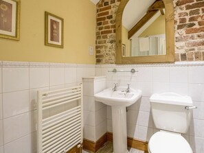 A bathroom with a white sink, toilet, and radiator. There are framed pictures on the wall and a mirror above the sink. - Manor Farm Barn (Dorchester)