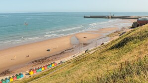 A beach with a pier, a lighthouse, and colorful beach huts. - Tyreman's Return (Whitby)