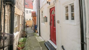 A narrow alleyway with a red door, white walls, and a small garden area with potted plants. - Tyreman's Return (Whitby)