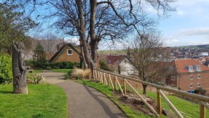 A paved path with a wooden fence on one side, surrounded by grass and trees. - Tyreman's Return (Whitby)