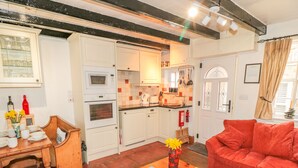 A cozy living room with a red sofa, a wooden coffee table, and a kitchen area with white cabinets and a microwave. - Tyreman's Return (Whitby)