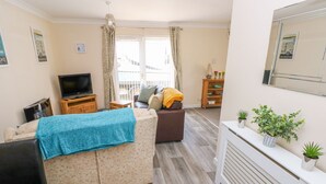 A cozy living room with a sofa, a TV, a small table, and a radiator. - Cranford Cottage (Pembroke)
