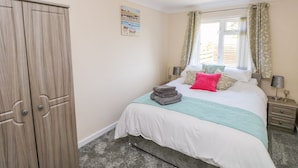 A bedroom with a bed, a wardrobe, a window with curtains, a bedside lamp, and a painting on the wall. - Cranford Cottage (Pembroke)