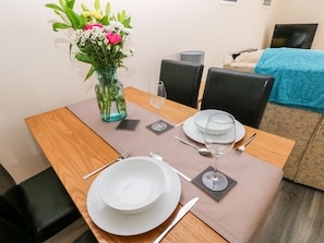 Une table à manger dressée avec de l’assiette blanche, des couverts et un verre d’eau, et un vase de fleurs placé sur la table.