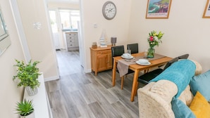 A modern living room with a wooden dining table, a sofa with cushions, and a kitchen in the background. - Cranford Cottage (Pembroke)