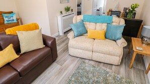 A living room with a brown leather sofa, beige sofa with blue and yellow cushions, a wooden coffee table, and a patterned rug. - Cranford Cottage (Pembroke)