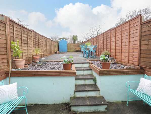 A garden with a wooden fence, a blue shed, and a seating area with a table and chairs.