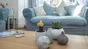 Un salon avec un canapé, des coussins, une table avec des magazines et des vases décoratifs.