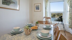 Un coin repas avec une table dressée pour quatre personnes, un télescope posé sur un trépied et une vue panoramique sur un lac, visible à travers de grandes fenêtres.