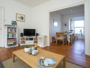Un salon comprenant un téléviseur, une bibliothèque, une table basse et un coin repas avec des chaises et une table.