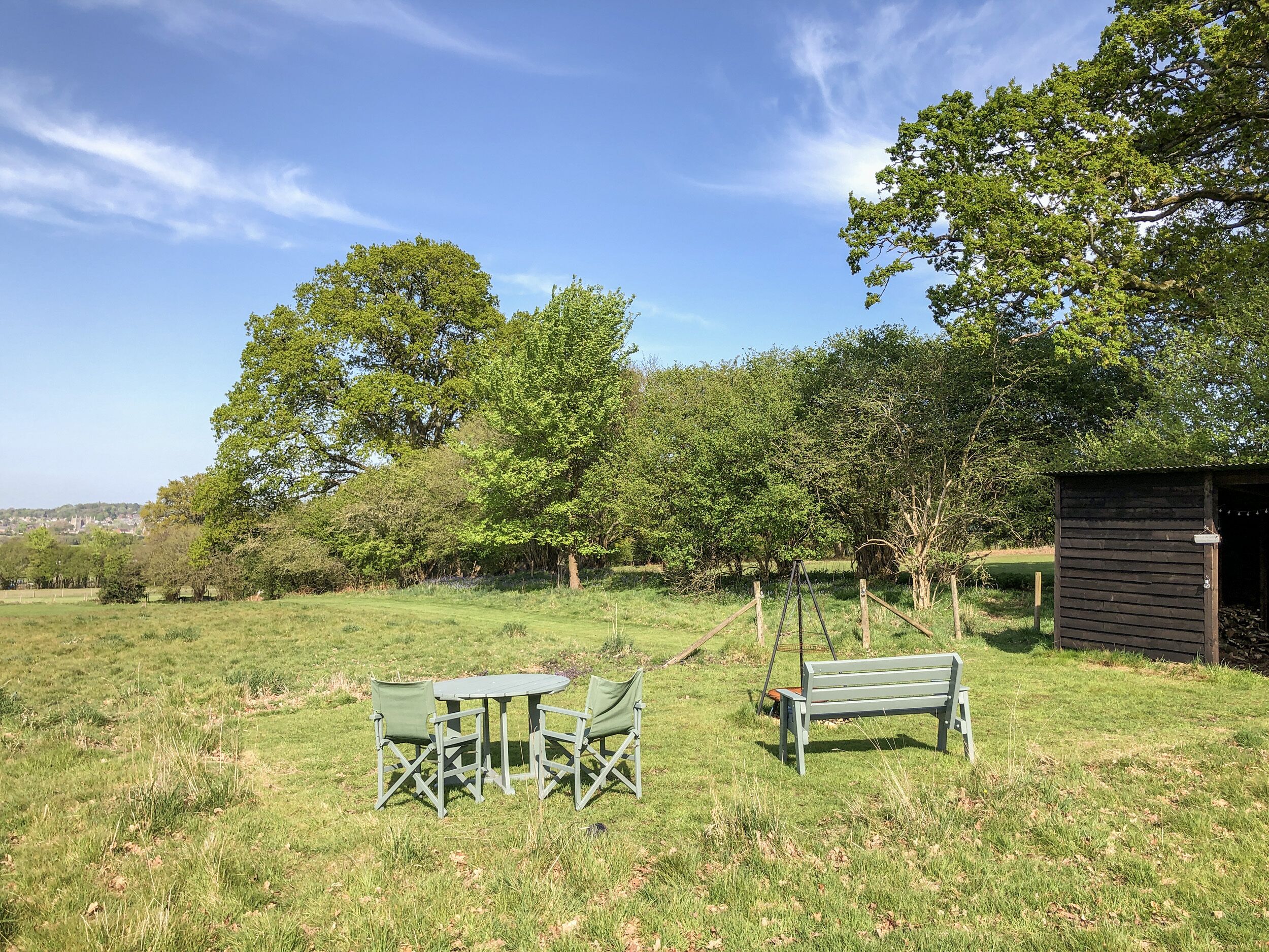A grassy outdoor area with a swing set, a small wooden structure, and a table with chairs.