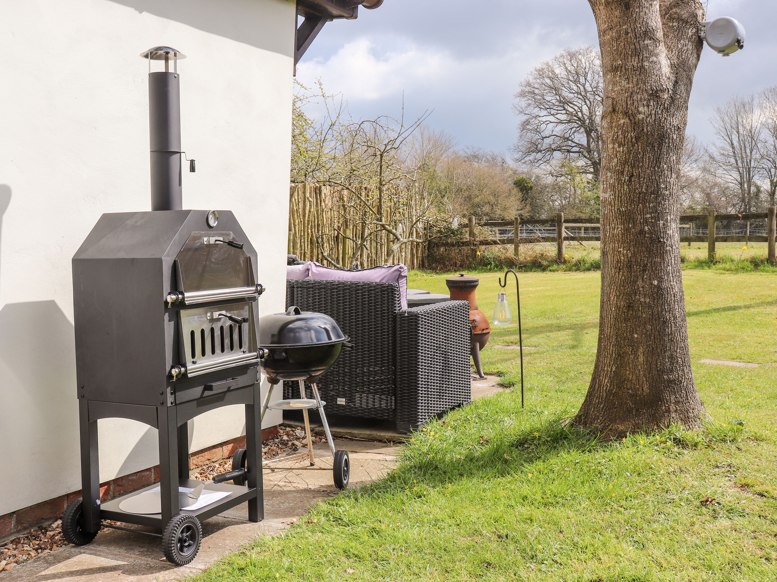 An outdoor grill setup next to a house with a tree and a fence in the background.
