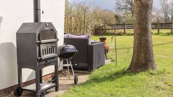An outdoor grill setup next to a house with a tree and a fence in the background.